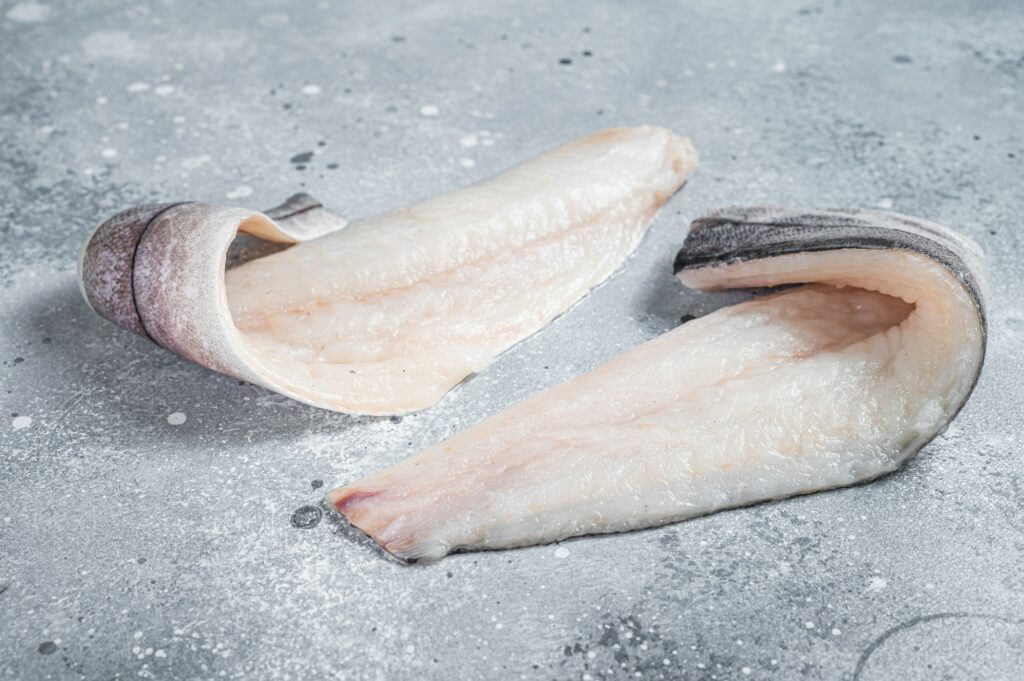 Two raw haddock fish fillets on kitchen table. Gray background. Top view